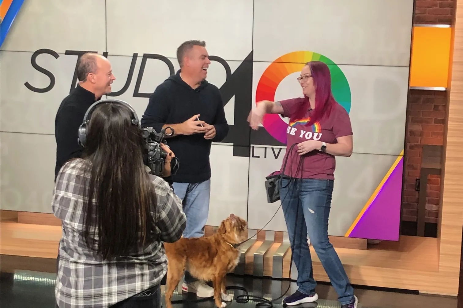 Terra with a dog on the Studio 40 news set in Sacramento, being interviewed by two hosts while a camera operator films the segment